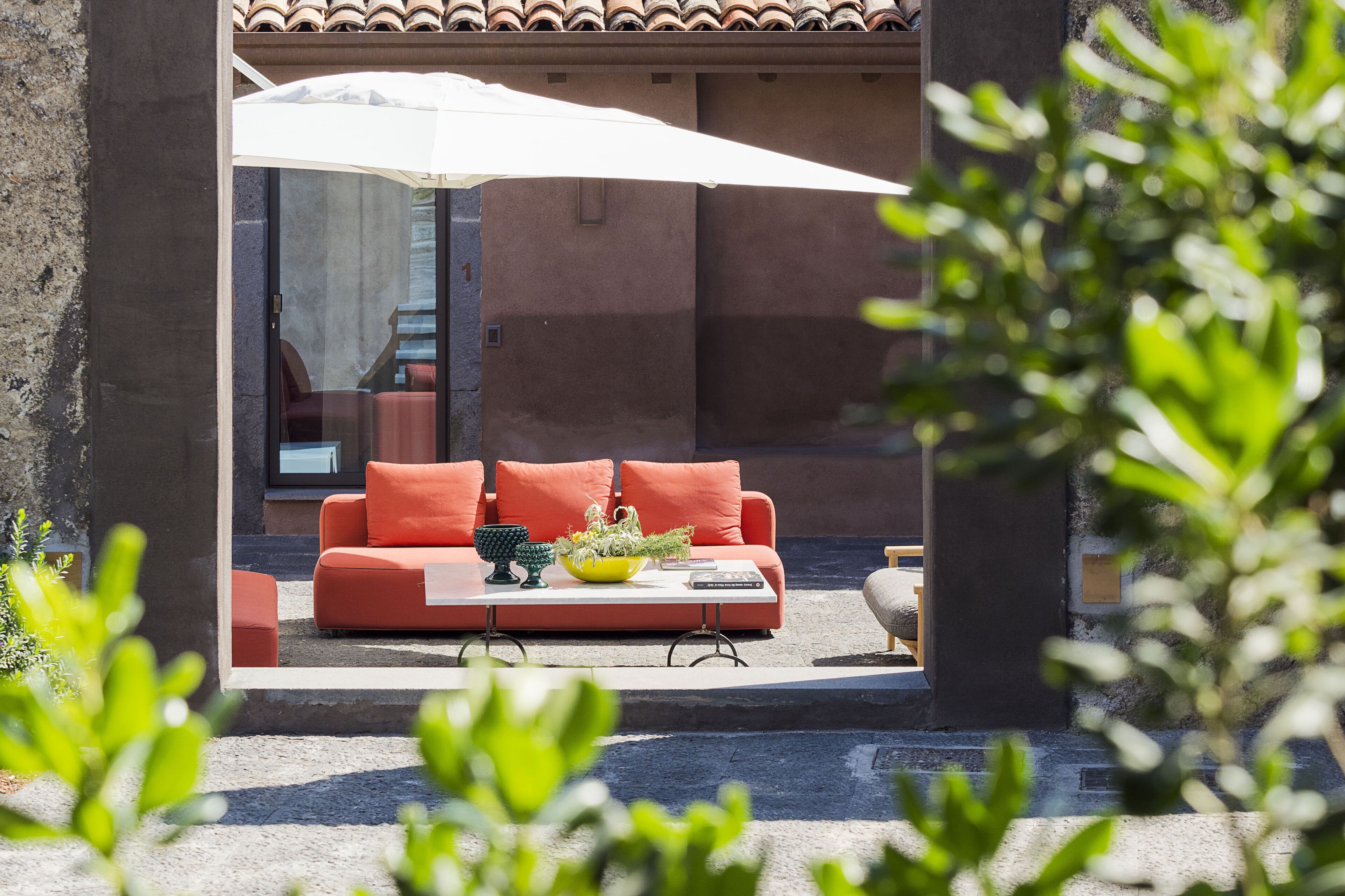 An outdoor seating area with a red sofa, a yellow bowl, and a white umbrella.