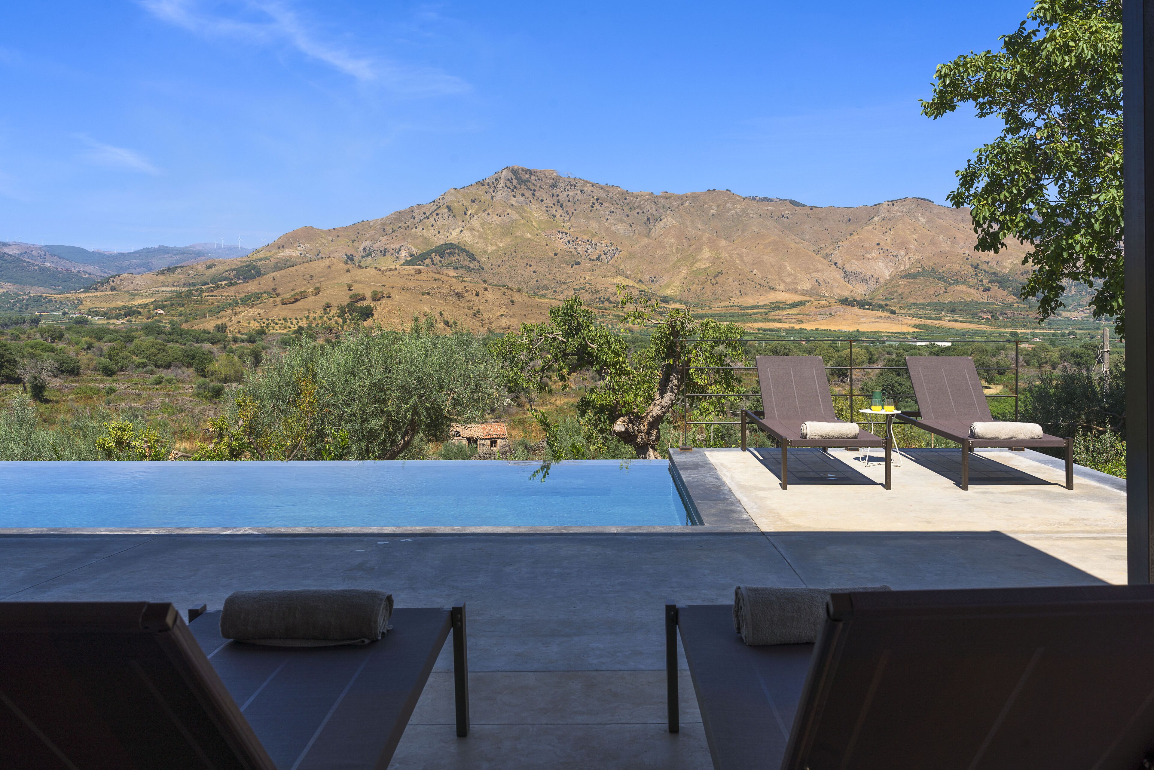 Área de piscina com espreguiçadeiras e vista para uma paisagem montanhosa.