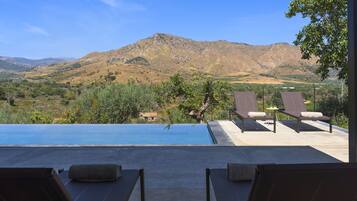Área de piscina com espreguiçadeiras e vista para uma paisagem montanhosa.