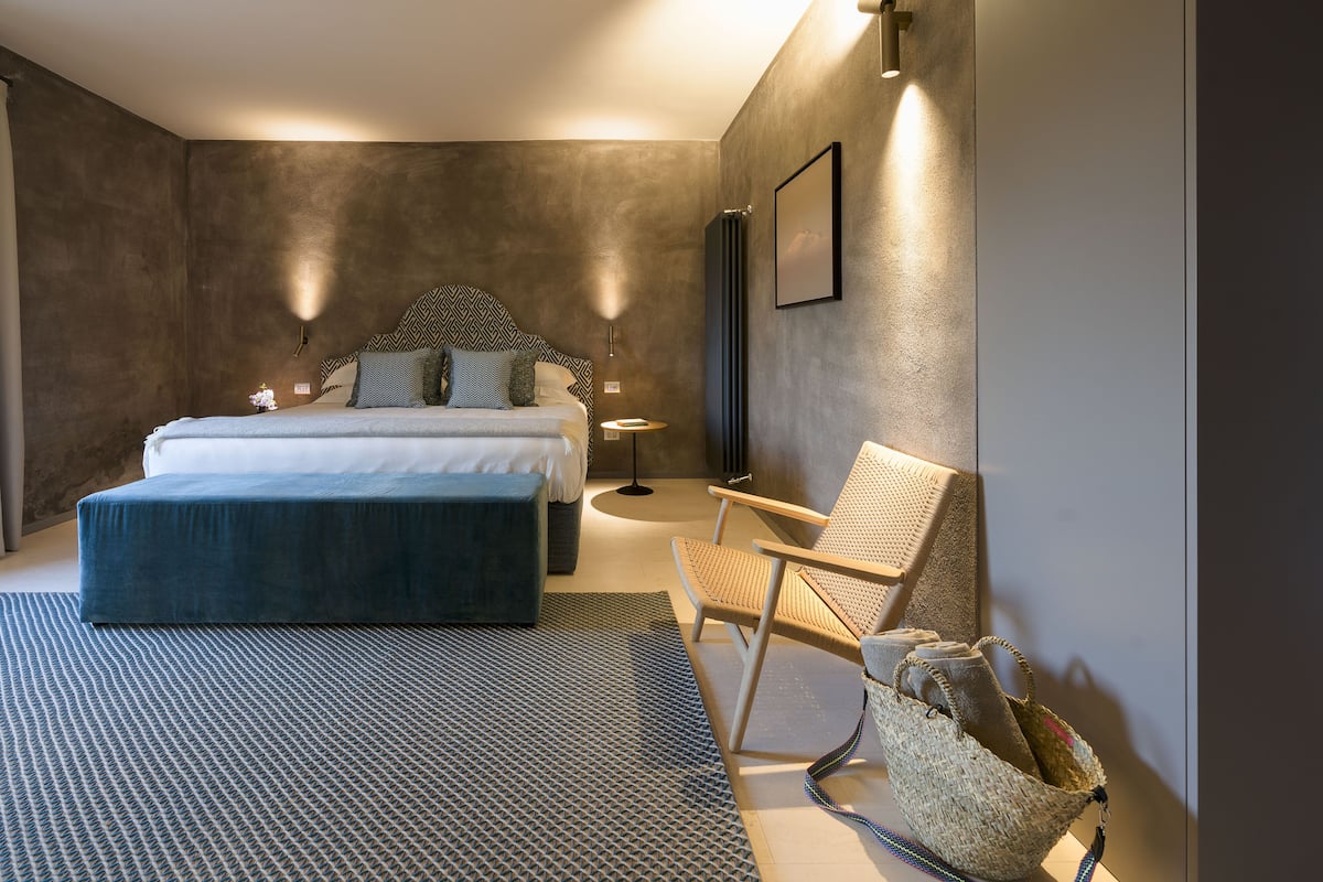 Een moderne slaapkamer met een groot bed, een stoel, een klein tafeltje en een wandlamp.