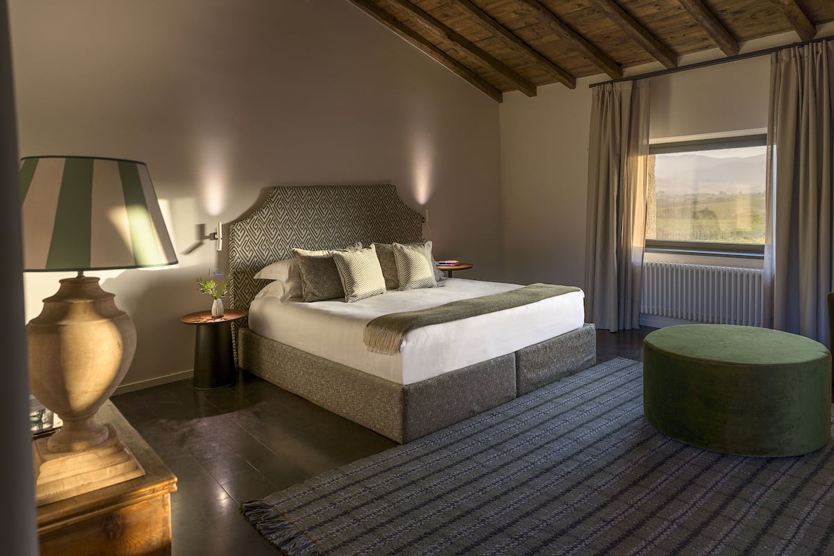 Een slaapkamer met een bed, nachtkastje, lamp en uitzicht op de omgeving.
