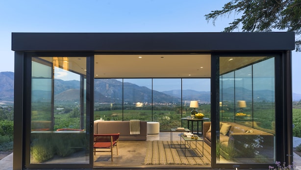 Un interior moderno con sofá, sillas y una mesa, con amplias paredes de vidrio y vistas al exterior.