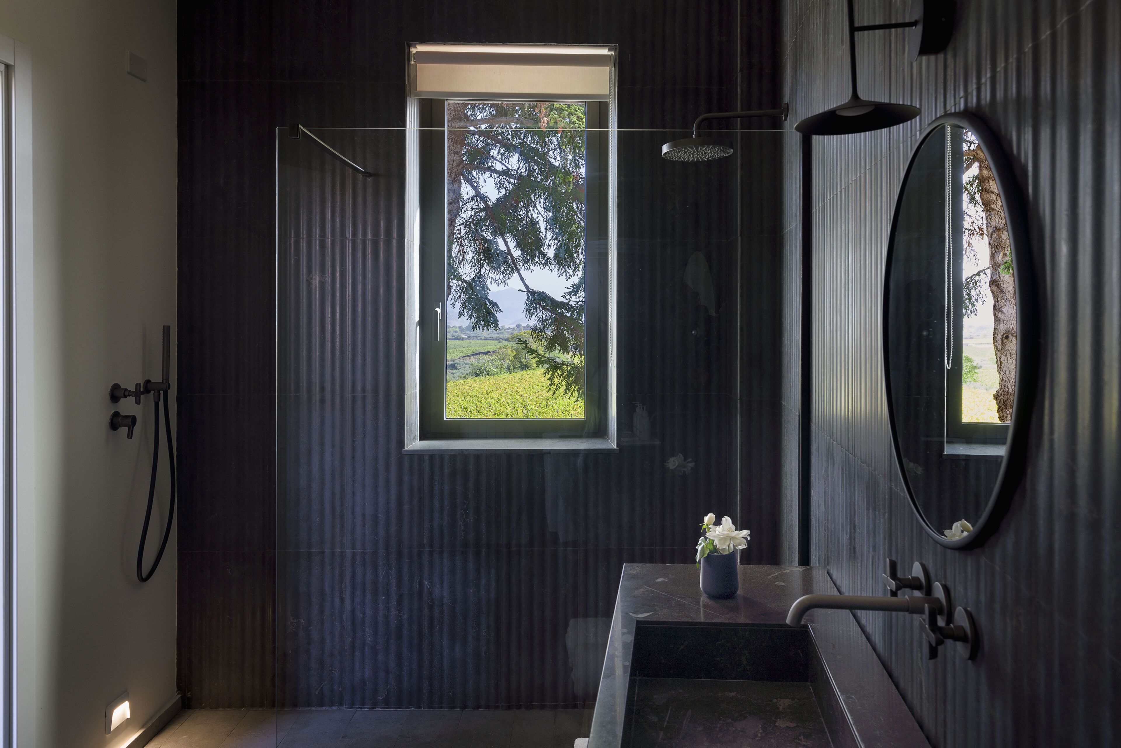 A modern bathroom with a glass shower enclosure, a small sink with a vase of flowers, and a large mirror.