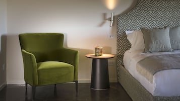 Una camera moderna con una poltrona verde, un tavolino rotondo con una lampada e un letto con lenzuola fantasia.