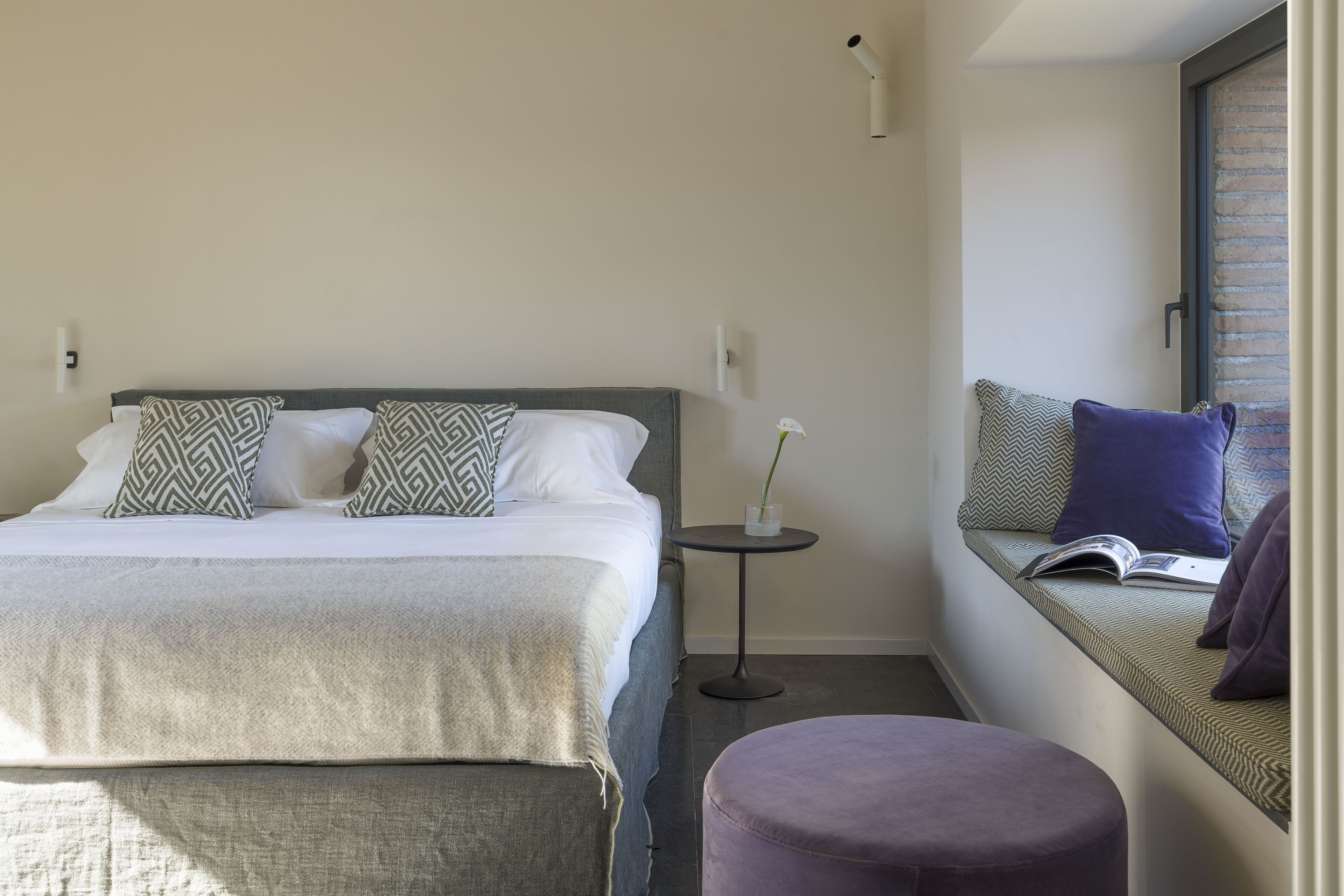 A modern bedroom with a bed, bedside table, and a reading nook with a bench.
