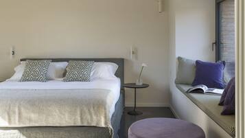 A modern bedroom with a bed, bedside table, and a reading nook with a bench.