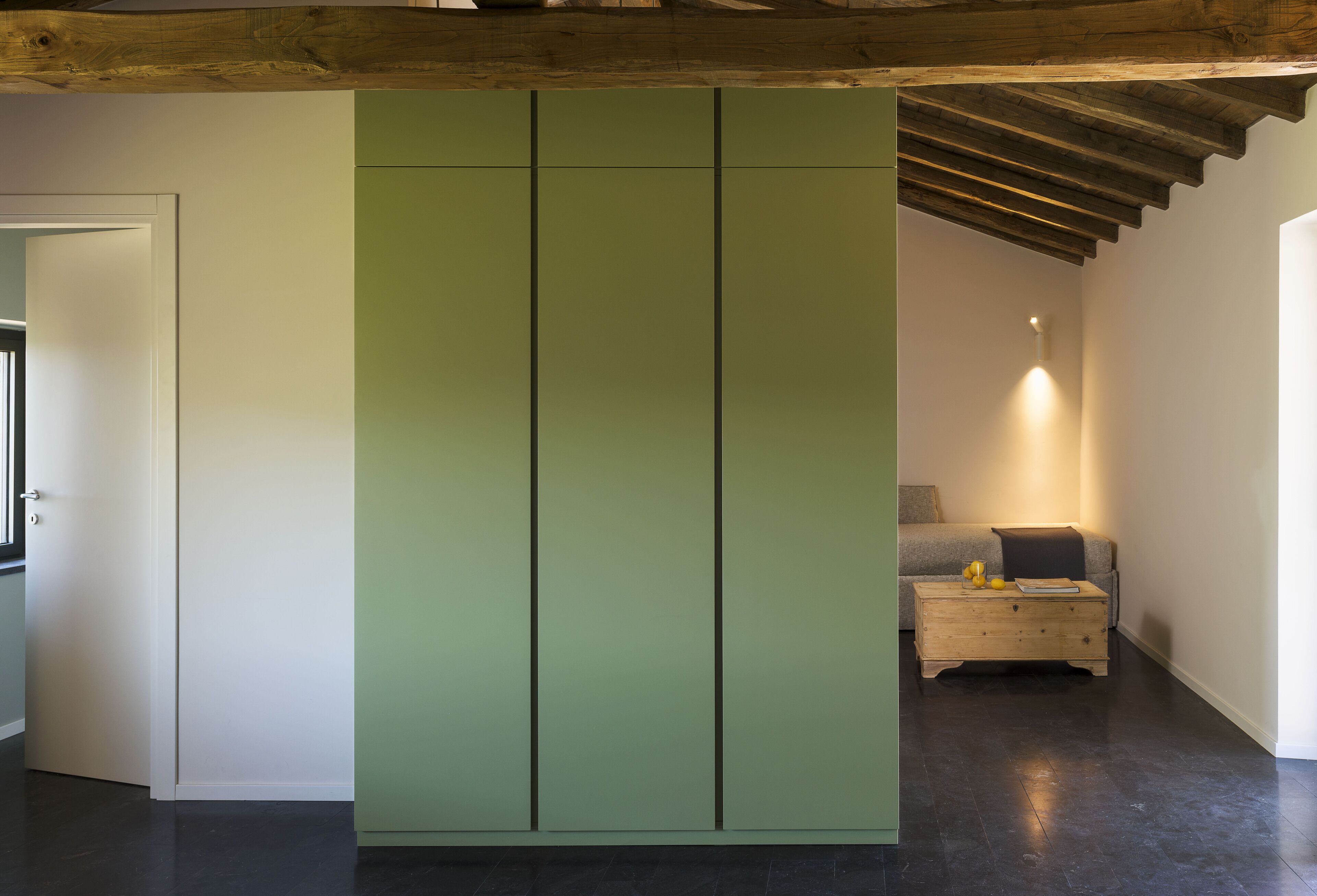 Una habitación con un armario verde, un banco de madera y un sofá.