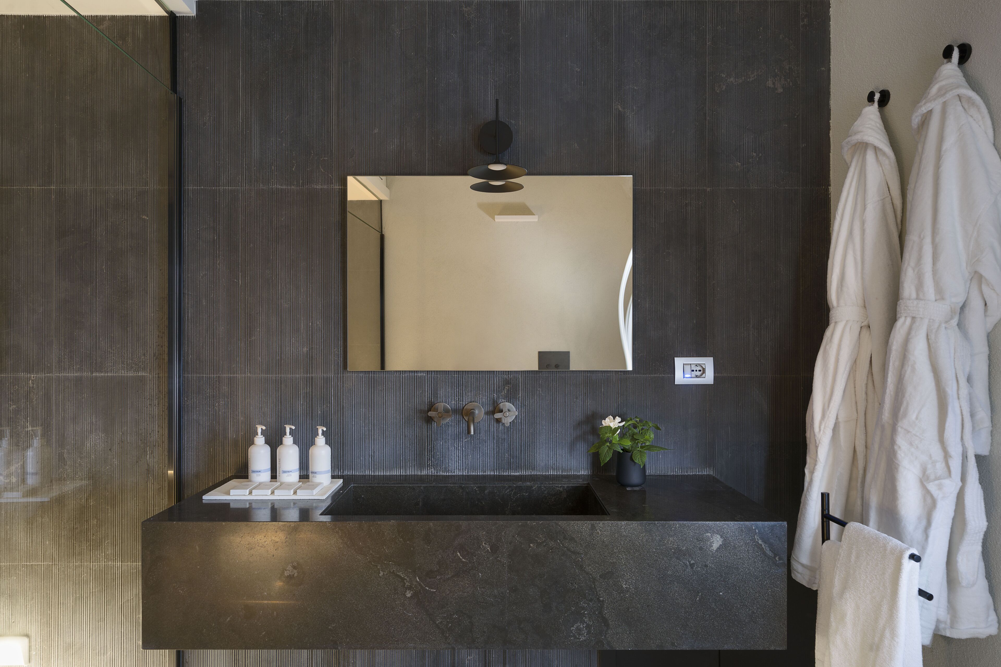 A modern bathroom with a dark marble sink, a large mirror, and two white towels hanging on hooks.