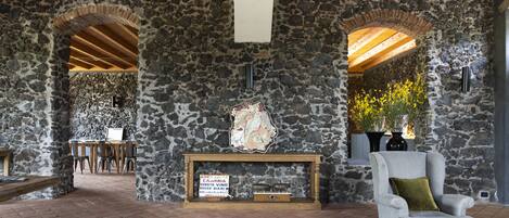 A stone-walled room with a fireplace, a wooden bench, and a chair with a cushion.