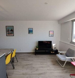 Una sala de estar con televisor, un comedor con sillas amarillas y un ventanal.