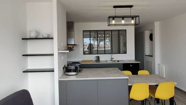 Una cocina moderna con una isla central, sillas amarillas y encimera gris.