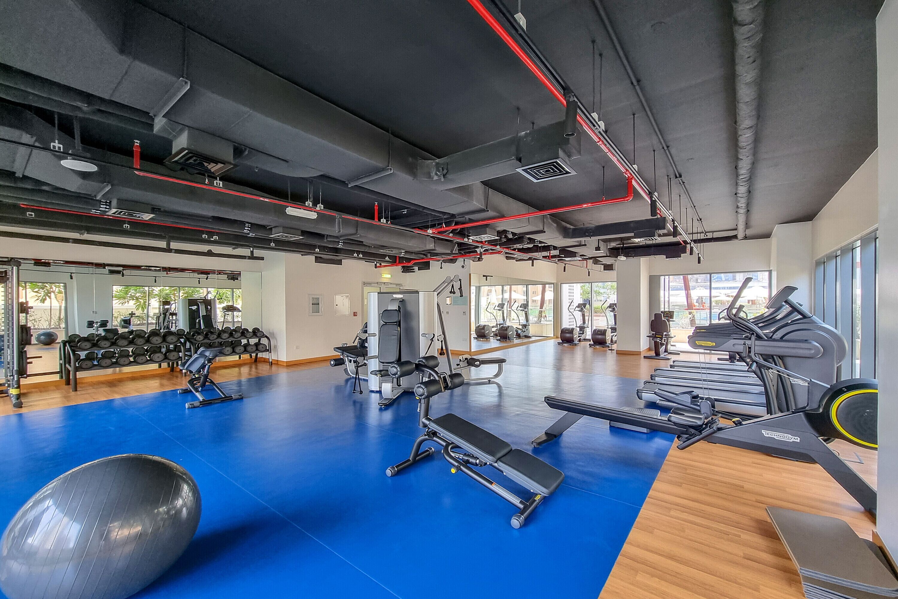 A gym with exercise equipment, a blue floor, and large windows.