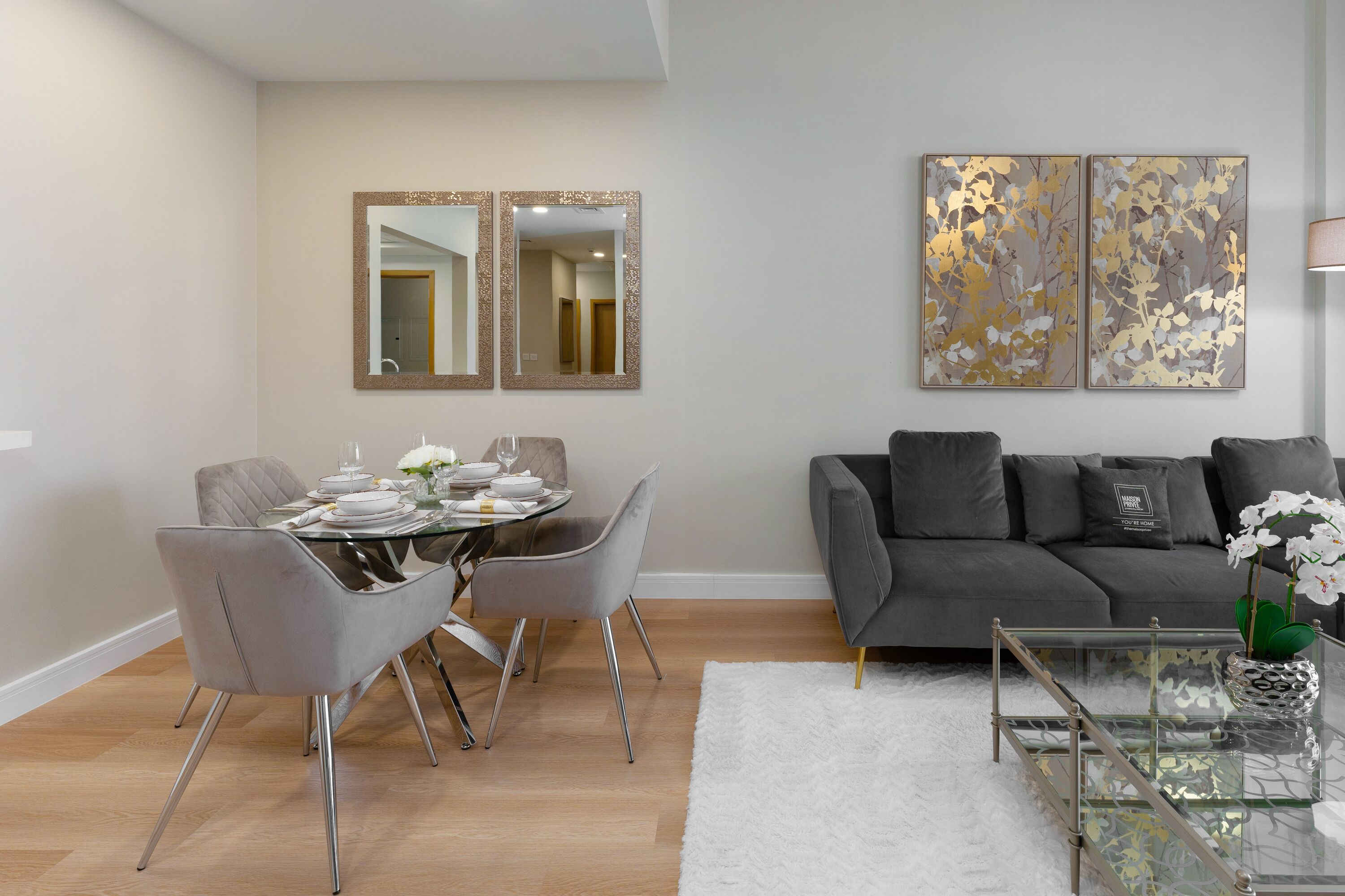 Un salon moderne avec un coin repas, comprenant un canapé gris, une table basse en verre et une table à manger dressée avec des assiettes et des verres.