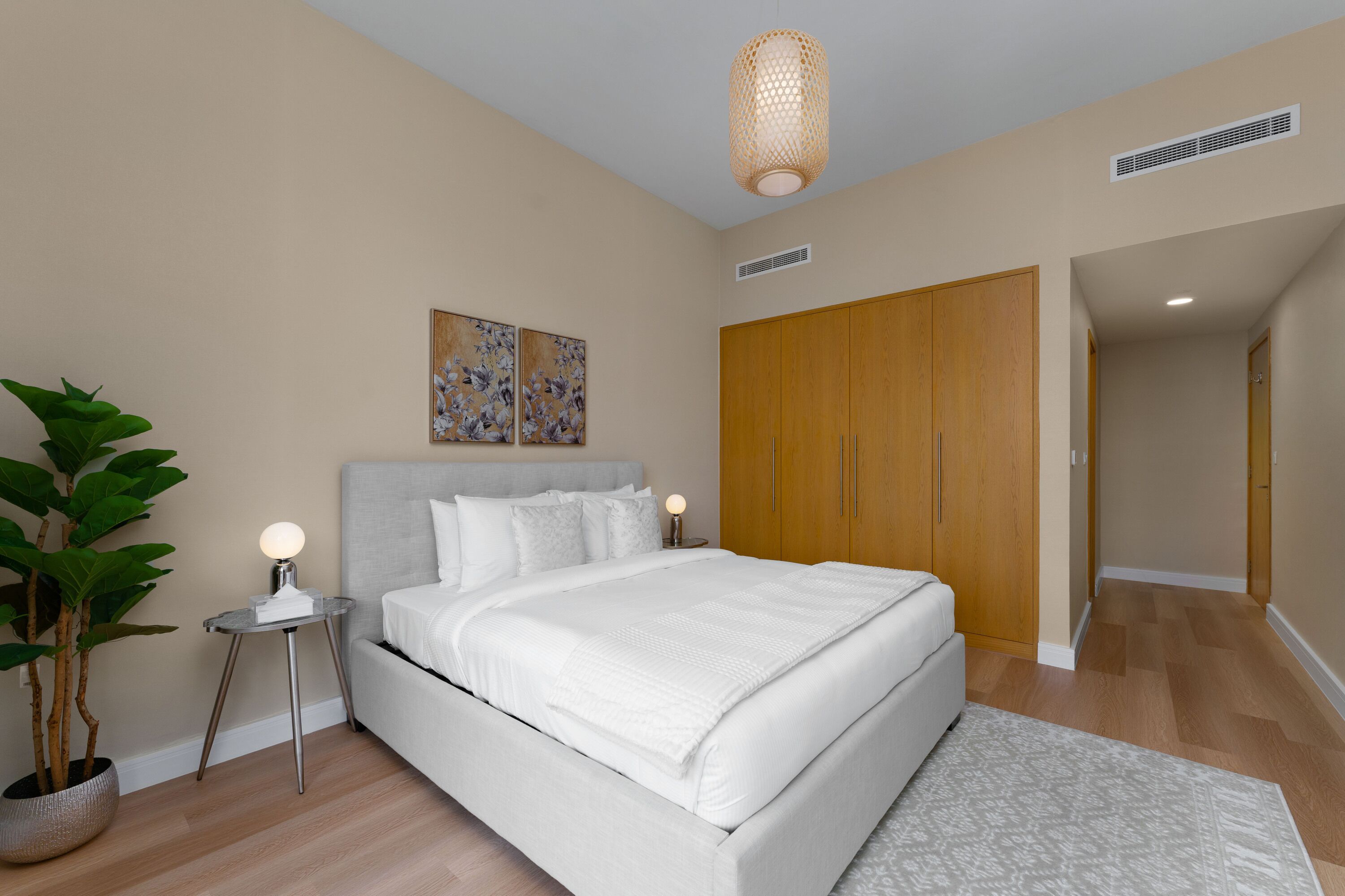Une chambre à coucher comprenant un lit, des tables de chevet, une plante en pot, des œuvres d’art accrochées au mur et une armoire.