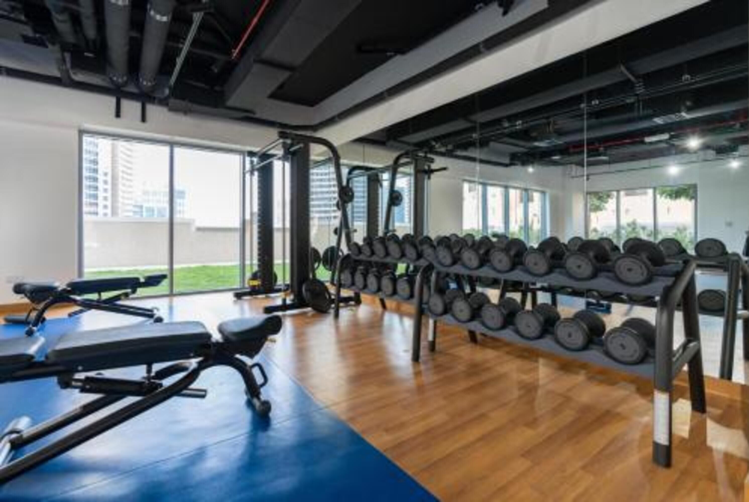 Een sportschool met trainingsapparatuur, rekken voor gewichten en grote ramen.