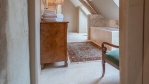 Een zolderkamer met een houten plafond, een kroonluchter, een badkuip en een groene stoel.