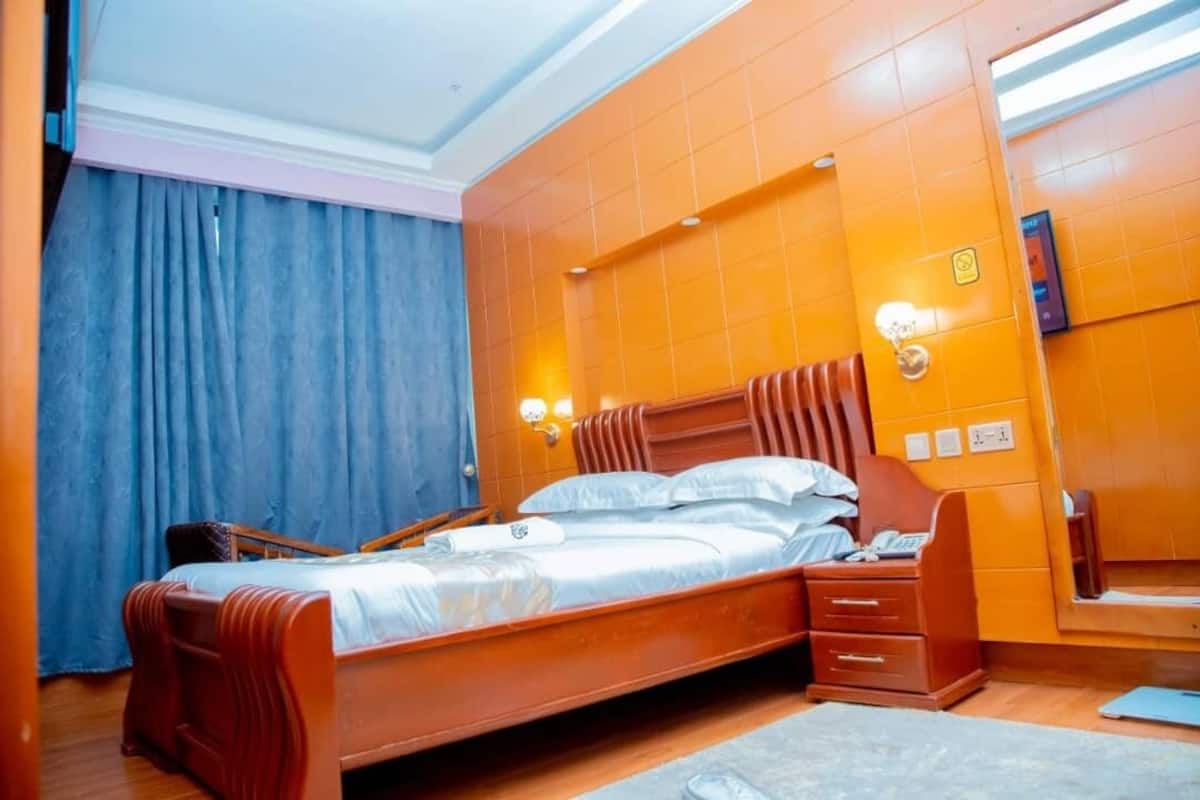 Una habitación de hotel con una cama de madera, una mesita de noche, un espejo y paredes con azulejos naranjas.