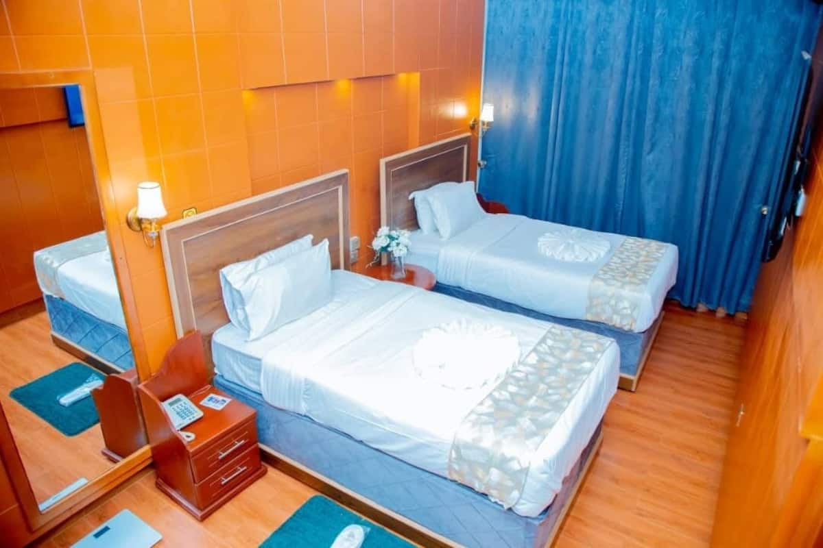 Una habitación de hotel con dos camas, una mesita de noche de madera, un espejo y una cortina azul.