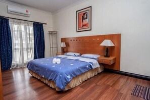 Quarto de hotel com cama de madeira, mesa de cabeceira com luminária, ar-condicionado fixado na parede e quadro emoldurado acima da cama.