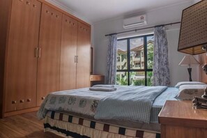 Ein Schlafzimmer mit einem Bett, einem Holzschrank, einem Fenster mit Vorhängen und einer Lampe.