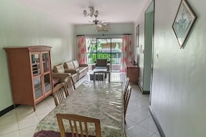 Ein Essbereich mit einem langen Tisch, Stühlen, einem Schrank, einer Couch und einem Deckenventilator.