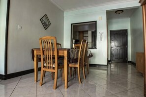 Uma sala de jantar com uma mesa e cadeiras, uma cozinha ao fundo, e uma porta que dá para outro cômodo.
