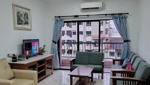 A living room with a sofa, a coffee table, a TV on a stand, and a window with curtains. - Nana Marina Court (Kota Kinabalu)