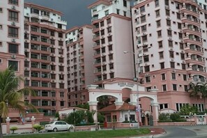 Un immeuble résidentiel à plusieurs étages, doté de balcons, d’une entrée principale et d’une voiture garée devant.