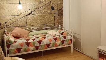 A bedroom with a stone wall, a bed with a patterned bedspread, a white metal headboard, and a small heater.