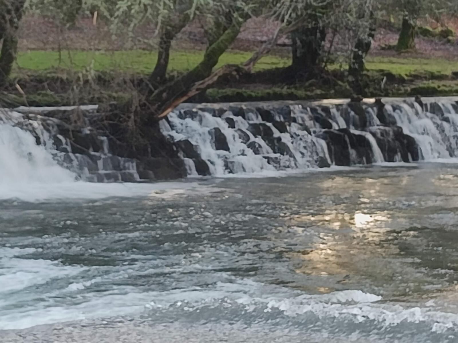Een waterval stort neer over een rotsachtige richel in een rustig waterbassin.