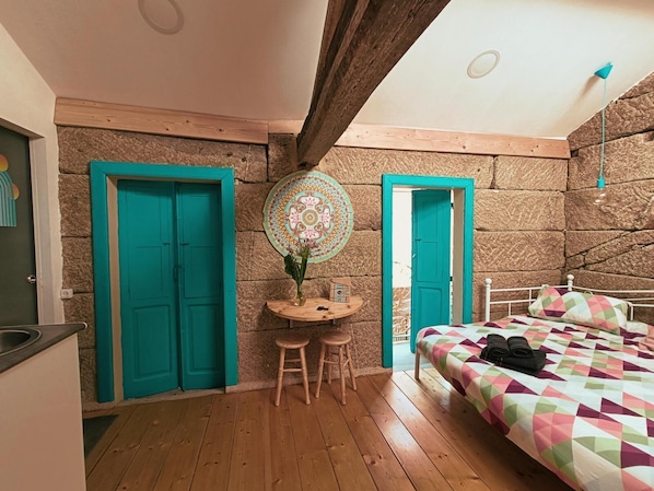 A room with a bed, a small table with stools, and two doors.