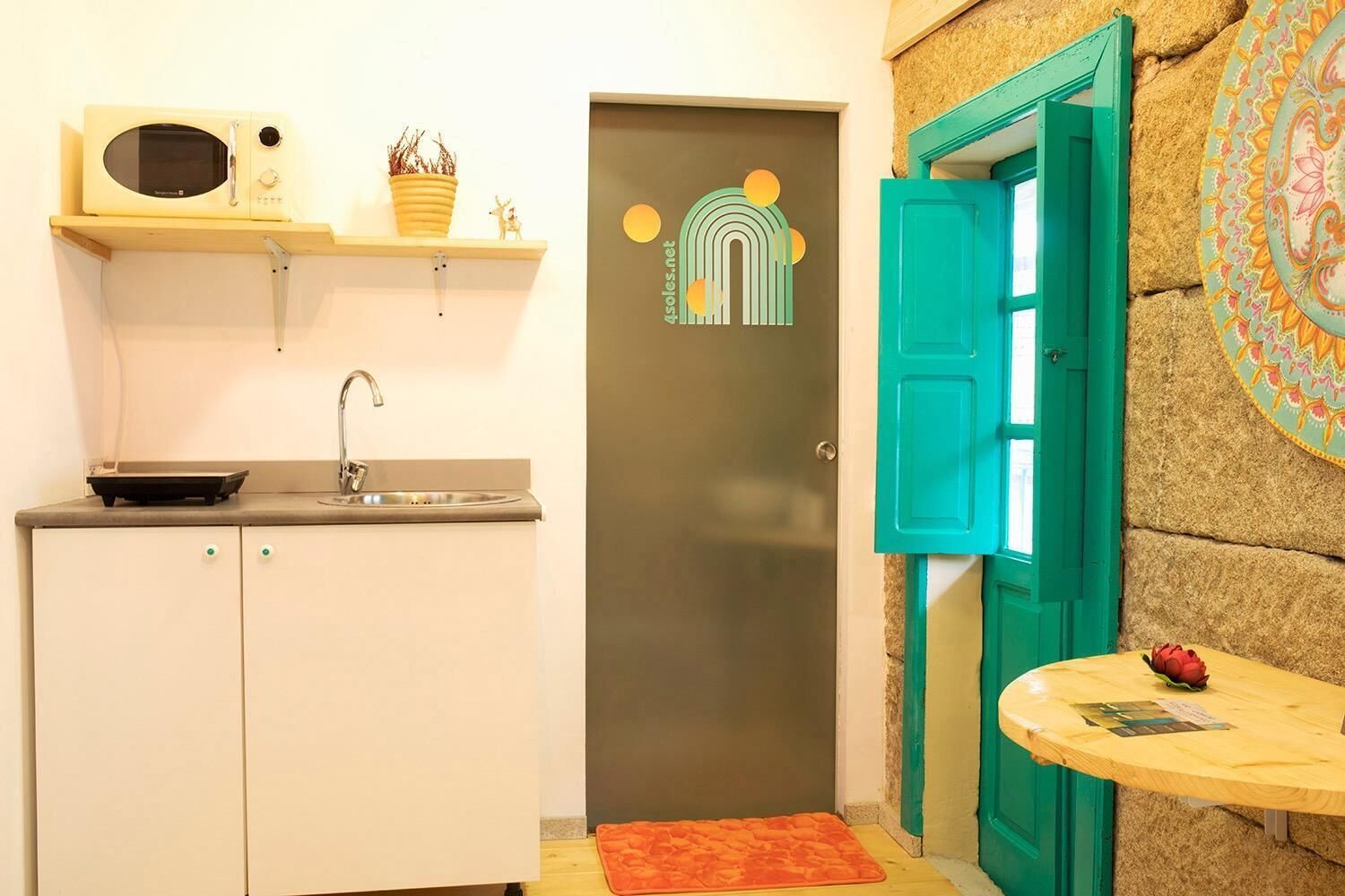 A compact kitchen with a microwave, sink, and a small table with a red object.