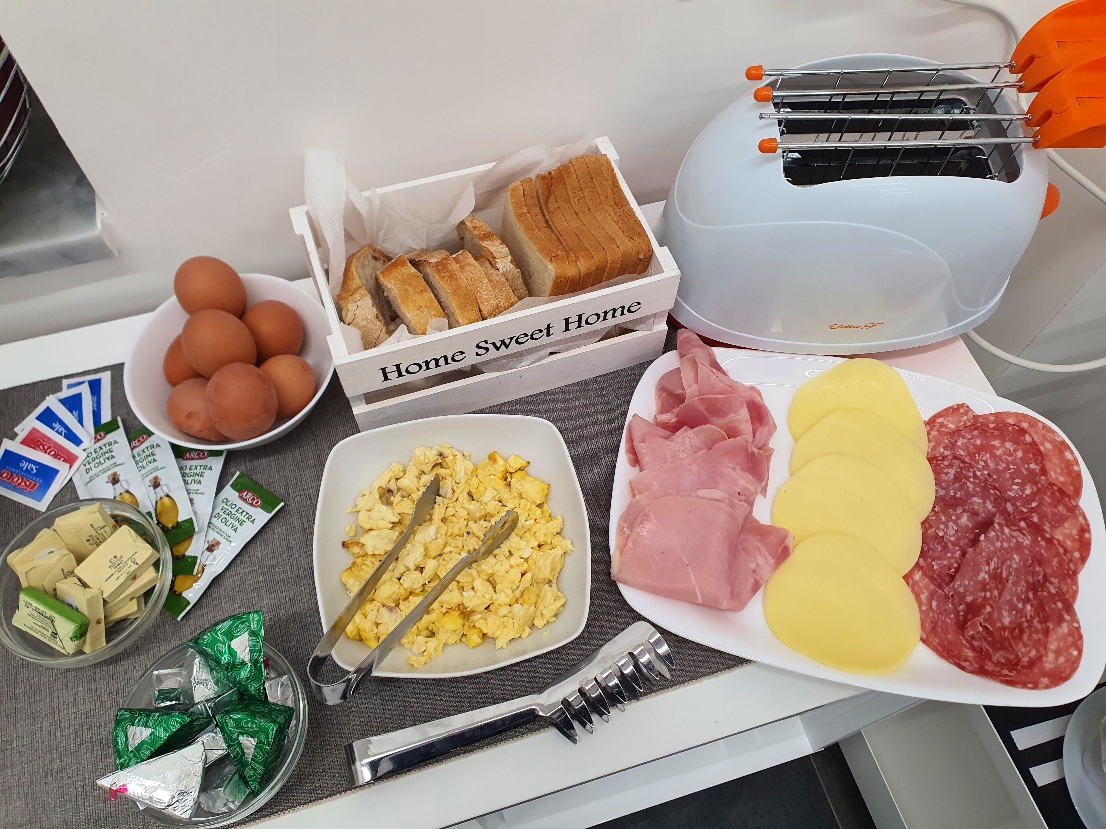 Ein Frühstückstisch mit Brot, Eiern, Schinken, Salami und Rührei.