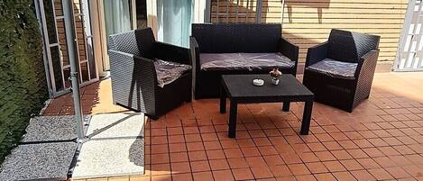 An outdoor patio with a tiled floor, a large umbrella, and three wicker chairs.