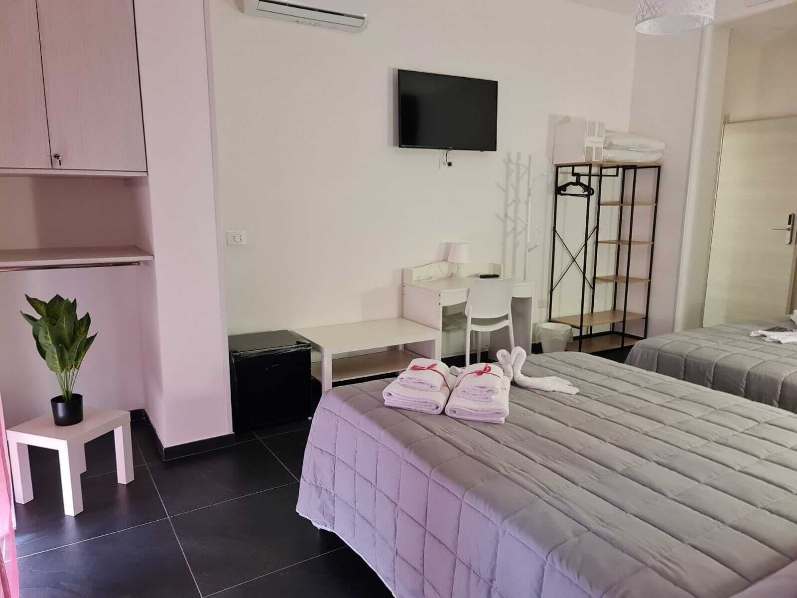 Une chambre d’hôtel avec deux lits, un bureau, une chaise, une télévision, une armoire et une plante.
