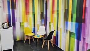 Un espace de bureau moderne avec un mur rayé aux couleurs vives, deux chaises jaunes, une table blanche et une chaise noire.