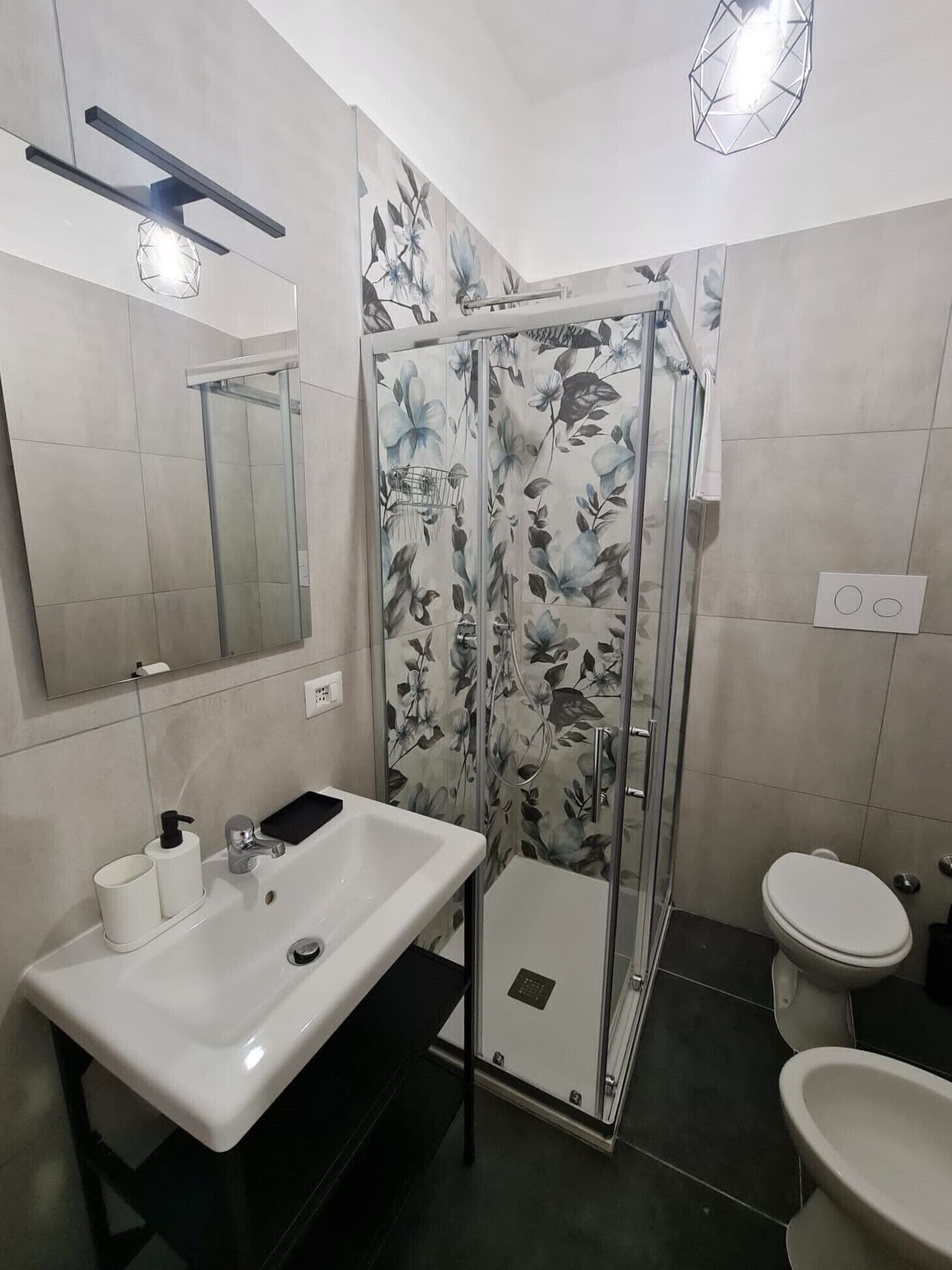A modern bathroom with a glass shower enclosure, a white sink with a black soap dispenser, and a toilet.