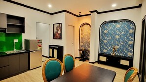 A compact kitchen with modern appliances, a dining area with teal chairs, and a decorative blue patterned wall. - An Living (Ho Chi Minh City)