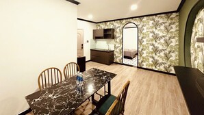 A compact room with a dining table and chairs, a small kitchenette, and a bed with a patterned wall. - An Living (Ho Chi Minh City)