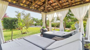 A covered outdoor seating area with cushioned loungers and a pergola overhead. - Petit Bijouc by Rentallorca (Can Picafort)