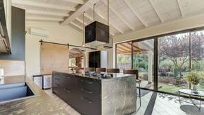 A modern kitchen with a large island, built-in appliances, and a view of the garden. - Petit Bijouc by Rentallorca (Can Picafort)