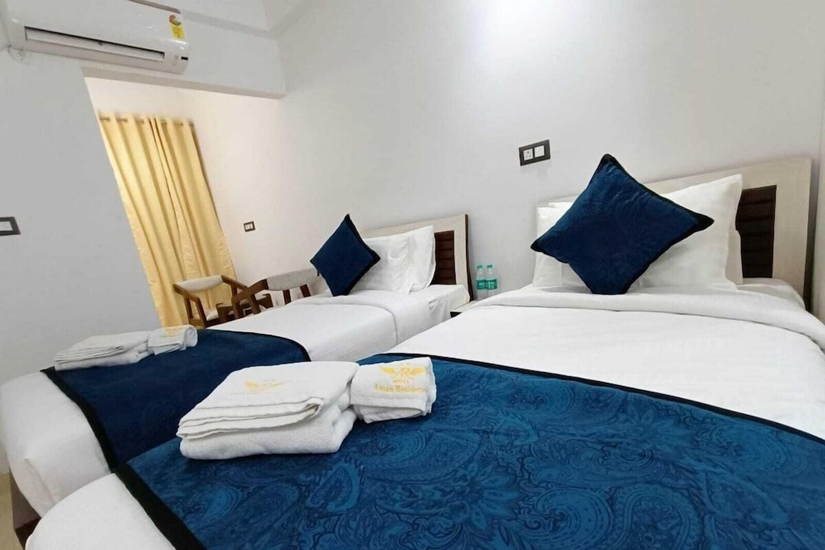 A hotel room with two beds, each with a blue bedspread and white linens. There is a chair and a small table with a bottle of water.