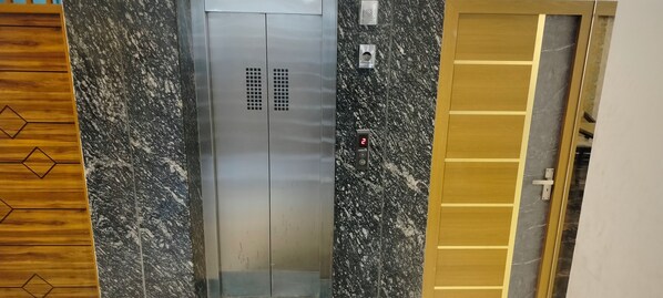 Um elevador com painel digital, parede de mármore e painel de madeira.