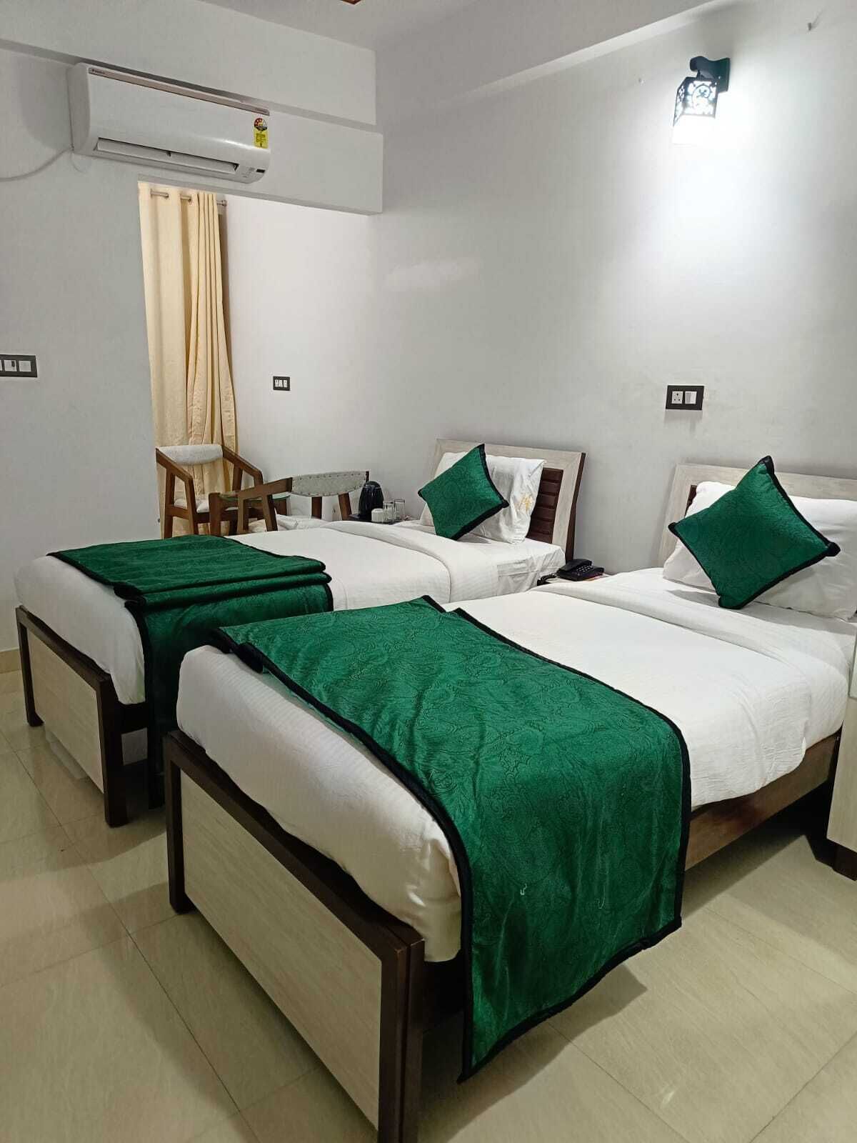 A hotel room with three beds, a chair, an air conditioning unit, and a small table.