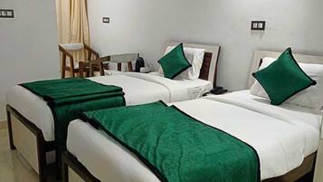 Habitación de hotel con tres camas, una silla, un aire acondicionado y una mesita.