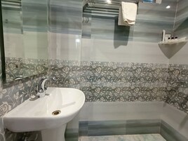 Un baño con un lavamanos blanco, cabina de ducha con paredes de vidrio y un papel tapiz con motivos florales.