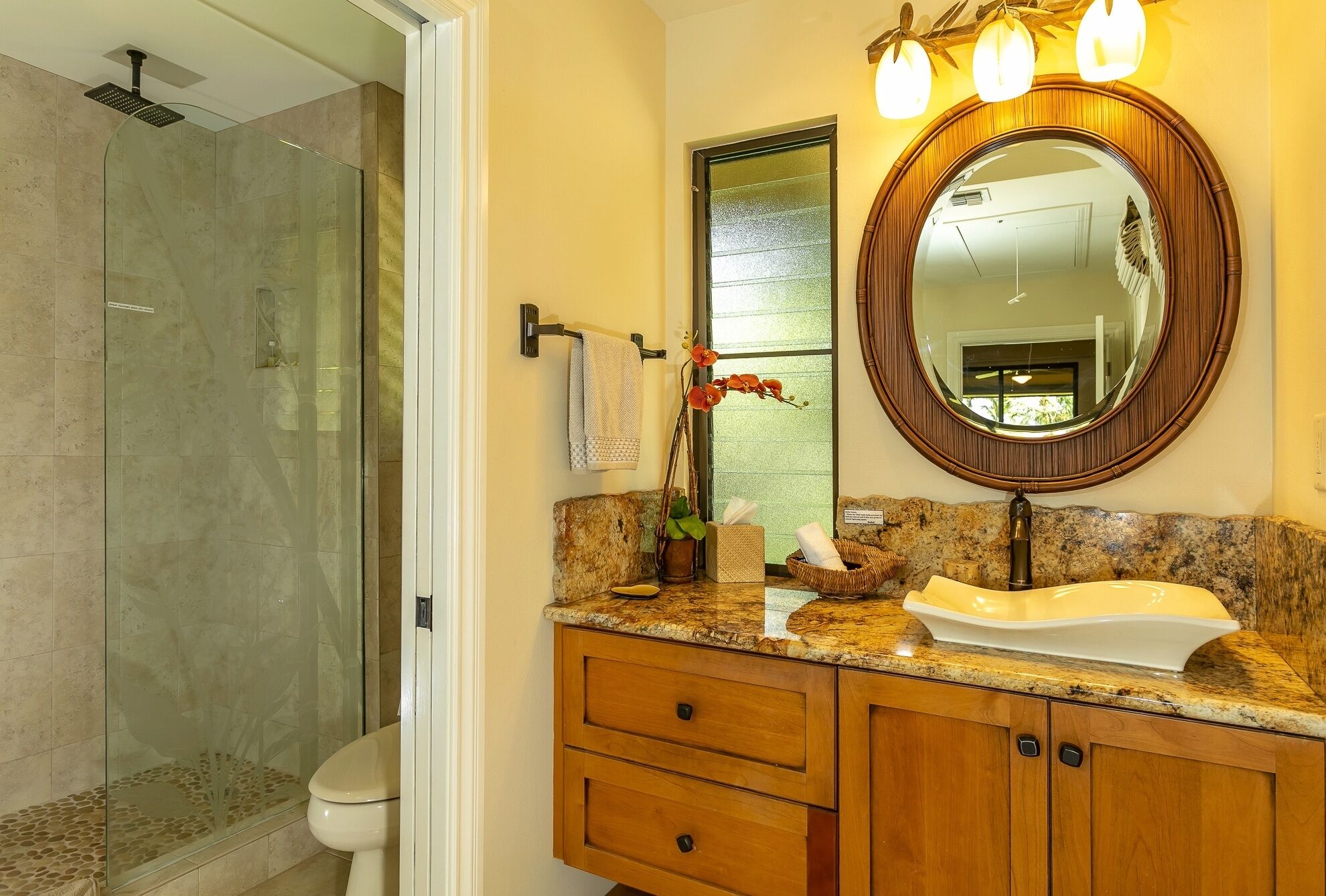 A bathroom with a glass shower enclosure, a white sink with a wooden vanity, and a large mirror with lights above it.