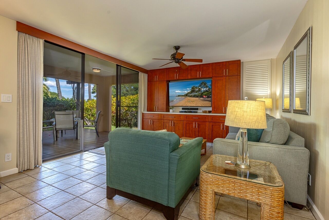 A living room with a television, a ceiling fan, and a view of the outdoors.