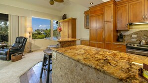 A kitchen with granite countertops, wooden cabinets, a stone backsplash, and a ceiling fan. - Wailea Ekahi One Bedrooms - Ocean View by Coldwell Banker Island Vacations (Kihei)