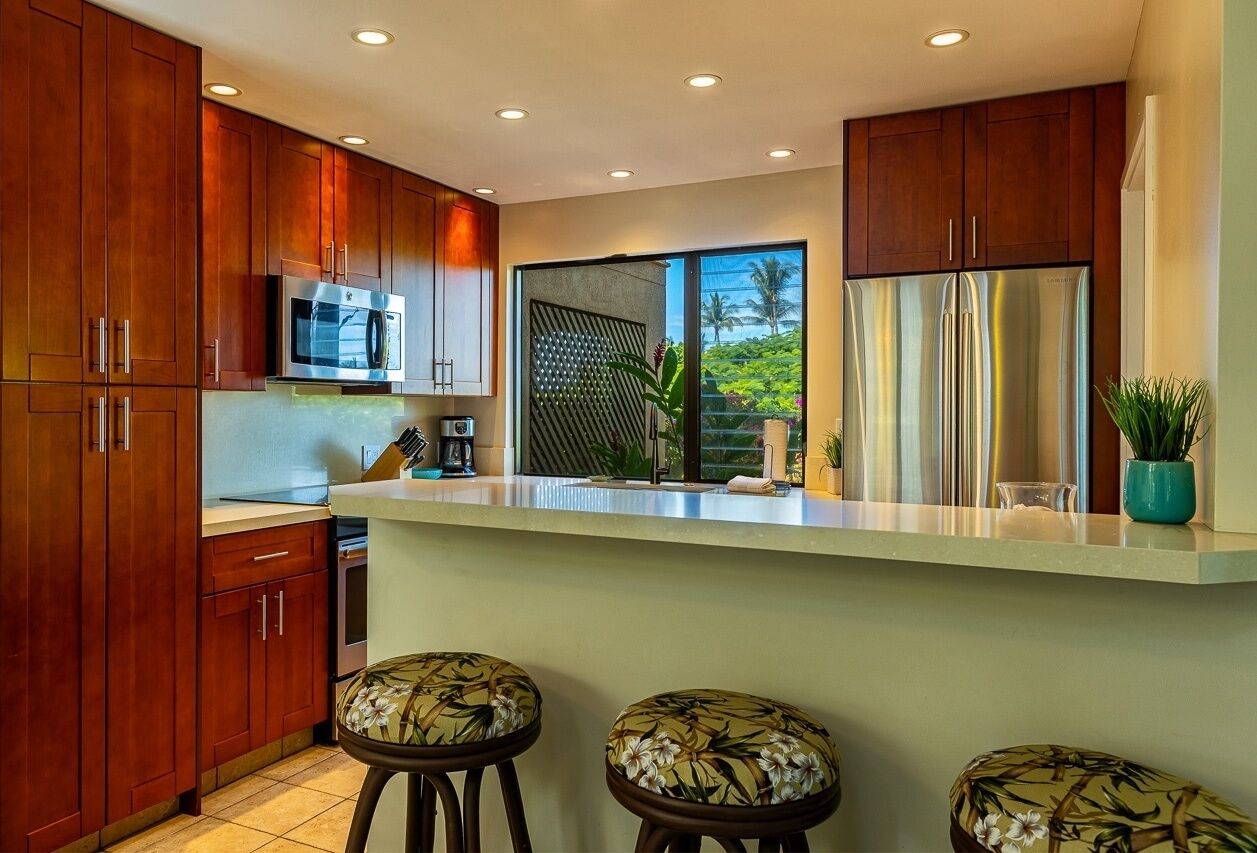 A modern kitchen with wooden cabinets, stainless steel appliances, and a large window offering a view of greenery.